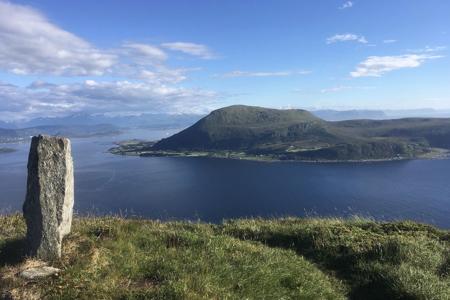 Utsikt mot fjord og fjell. Lettskya himmel i bakgrunnen